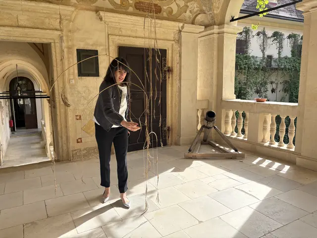 Kuratorin Alice Stori Liechtenstein bei einem besonderen Mobile auf einer der Schloss-Terrassen: Lorenzo Zerbini hat unter dem Titel "An Echo is the Whisper of an Absence" das Sterben des Mamutbaumes im Schlosspark thematisiert. Dazu hat er kupferne Sequoia-Nadeln nach dem Vorbild der bereits abgefallenen Baumnadeln in dieses Mobile verarbeitet und rückt damit das Gleichgewicht organischer Vergänglichkeit und der Frage nach dem Bewahren in den Fokus. | Foto: MeinBezirk/Susanne Veronik