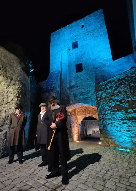 Drei Männer in historischer Kluft vor einem blau beleuchteten Turm