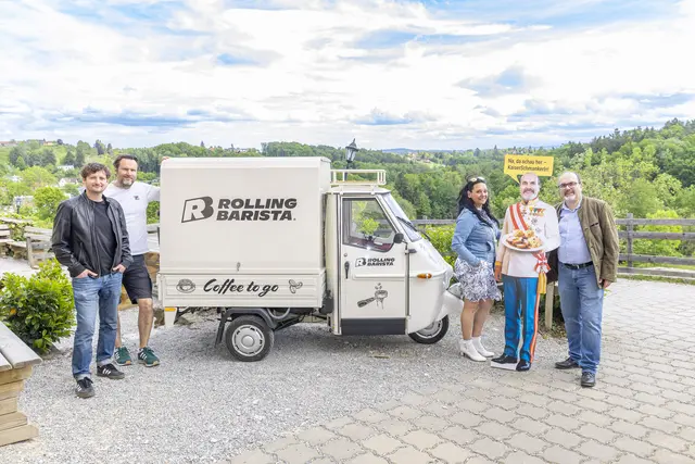 Vier Personen stehen um ein kleines Auto, in dem Kaffee gemacht wird, dahinter viel Natur.
