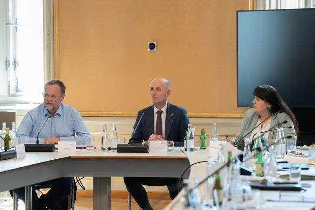 Drei Personen in formeller Kleidung nehmen an einer Sitzung teil.
