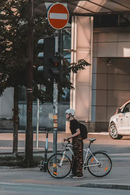 Eine Radfahrerin mit Helm steht an einer Ampel. 
