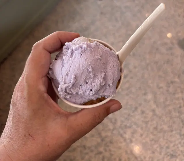 Hand mit Eisbecher, lila Eiskugel und Löffel von oben
