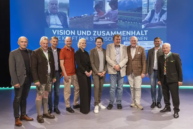 Einer Gruppe von Menschen steht im Halbkreis, dainter ein Plakat mit dem Titel der Dokiumentation.