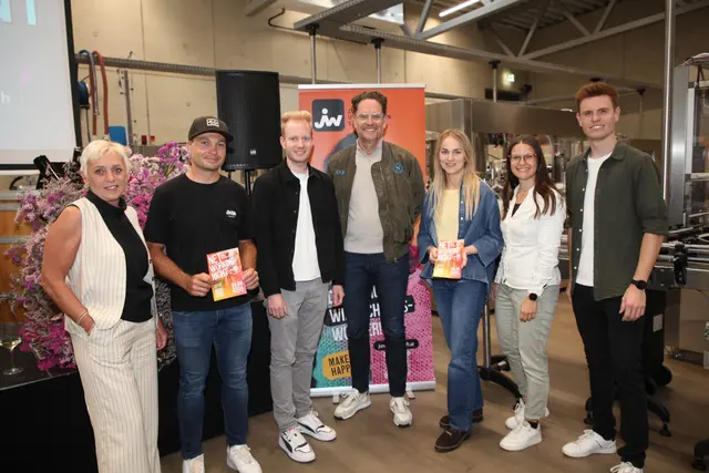Eine Gruppe von Menschen posiert in einer Produktionshalle für ein Gruppenbild.