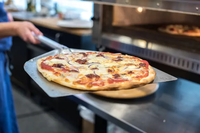 Pizza auf Blech wird aus dem Ofen geholt