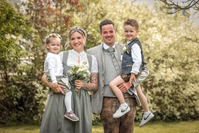 Ein Paar in Hochzeitstracht trägt seine Kinder auf dem Arm