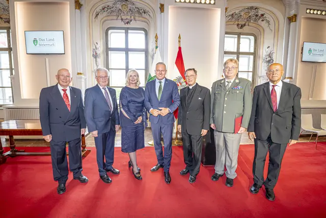 Eine Frau und sechs Männern stehen in einem historischen Raum.