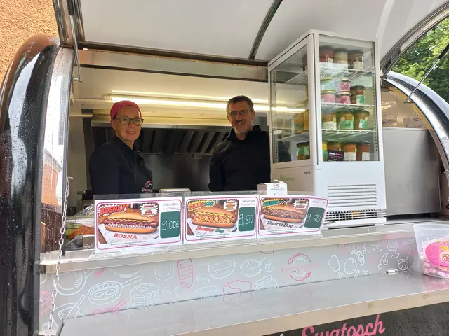 2 Menschen stehen hinterm Verkaufspult eines Hot-Dog-Standes