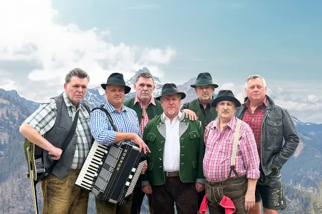 Musiker mit Instrumenten stehen vor Gebirgslandschaft