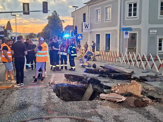 Fräsmaschine nach Straßeneinbruch auf der L568: Einsatzkräfte sichern die Baumaschine mit einem Kran, während die freigelegte Gasleitung auf mögliche Schäden überprüft wird. | Foto: FF Enns