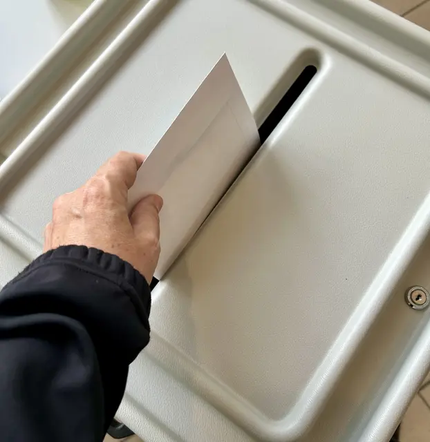 Hand mit Wahlumschlag vor Urne