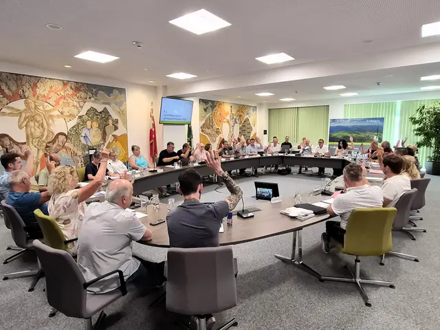 Gemeinderatsmitglieder sitzen am runden tisch und geben Handzeichen zur Abstimmung
