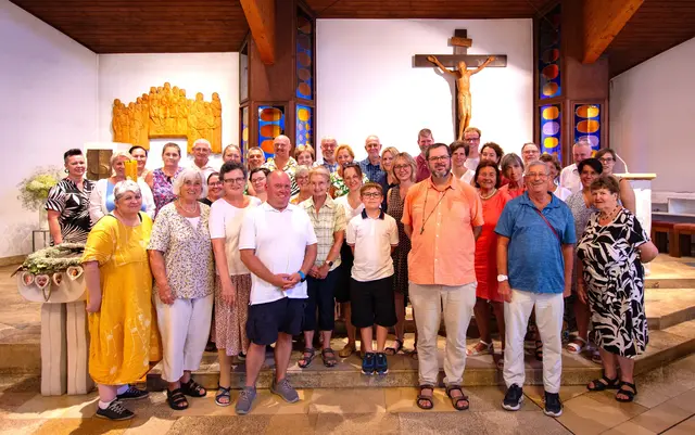 Gruppenfoto der gesamen Reisegesellschaft  im Altarraum des neuen Kirchenraumes mit dem Ortspfarrer Günter Maria Schweifer (erste Reihe unter dem Kreuz)