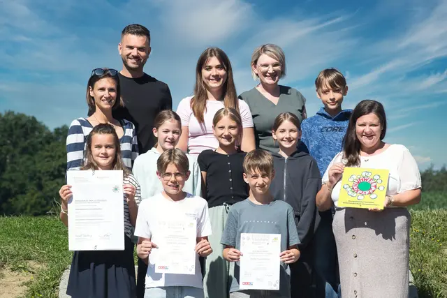 Eine Gruppe von Kindern und Erwachsenen halten Auszeichnungen in Richtung Kamera.
