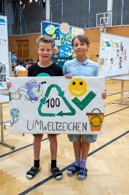 Zwei Buben halten ein großes, selbst kreiertes Umweltzeichen in Händen.