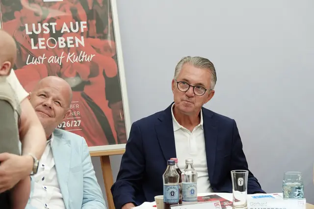 2 Männer sitzen an einem Tisch, davor stehen Getränke