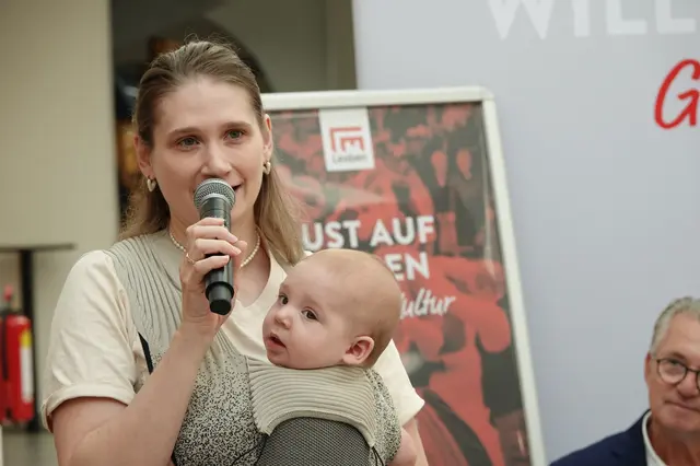 Frau spricht ins Mikrophon und hält ihr Baby am Arm