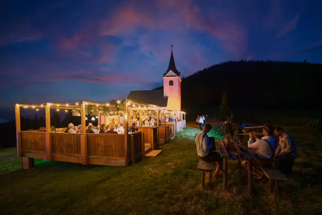 Gäste sitzen vor der Wallfahrtskirche Maria Schnee auf der Gleinalm bei einem Abendessen