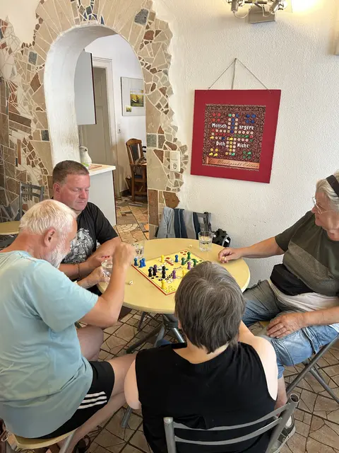 2 Männer und 2 Frauen sitzen am Tisch und spielen Mensch-ärger-dich-nicht
