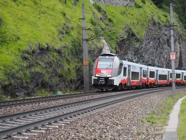 Rot-weißer ÖBB City Jet fährt auf einer Eisenbahntrasse entlang einer steilen Felswand mit Stützmauern.