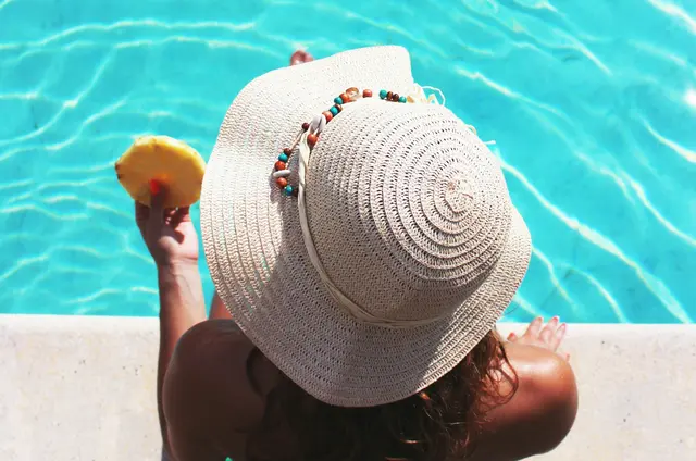 Frau mit Sonnenhut sitzt am Pool 