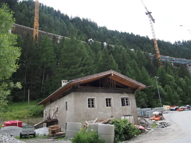 Gotisches Wohngebäude mit offen liegendem, hölzernem Dachstuhl auf einer Baustelle im Tal unter einer großen, teils neu zu errichtenden Autobahnbrücke.