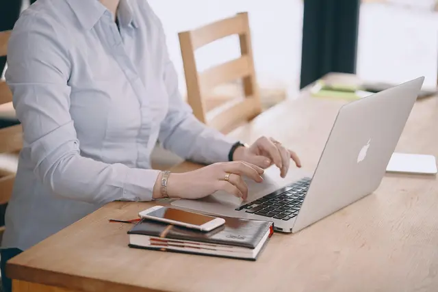 Frau sitzt vor Laptop mit Handy und Notizbuch