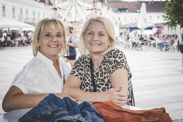 2 Frauen stehen an einem Tisch und lachen.