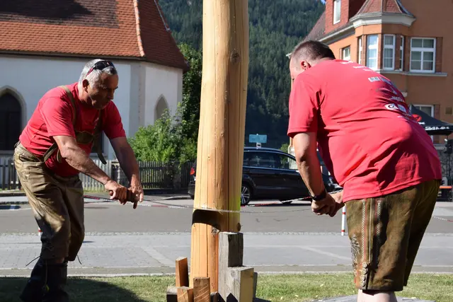 zwei männer schneiden mit einer Säge einen Maibaum um
