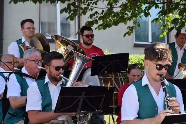 Mehrere Blasmusiker spielen auf ihren Instrumenten. Vor jedem steht ein Notenständer