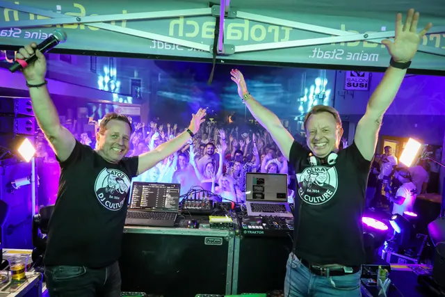 2 Männer stehen am Dj-Pult, dahinter feiert die Menge.
