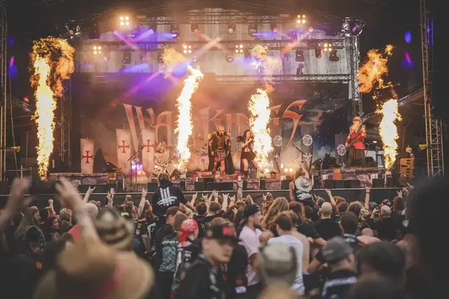 Eine Rockband spielt mit einer Feuershow auf einer Bühne vor vielen Zusehern