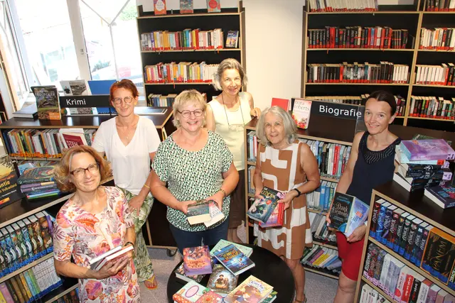 Eine Gruppe Frauen hat sich zwischen Bücherregale gestellt.
