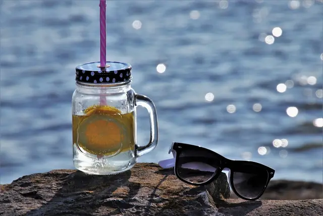 Glas mit Strohhalm gefüllt mit Wasser, daneben liegt eine Sonnenbrille