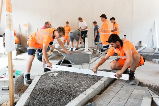 Zwei junge Männer arbeiten an einem Modell einer Straßenbaustelle.