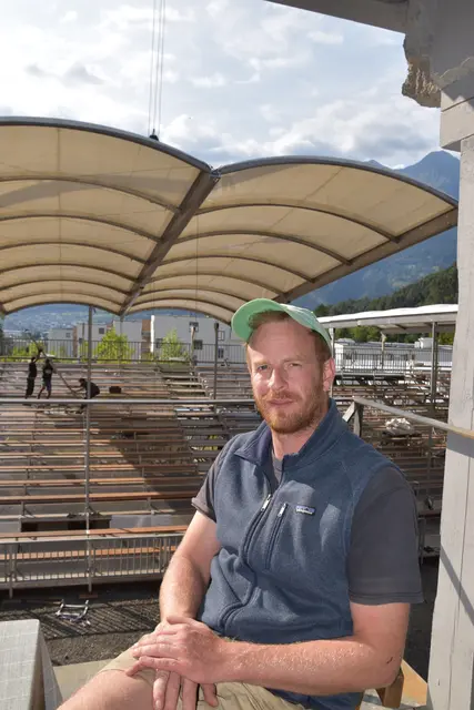 Technischer Leiter Tobias Hartung steht im geöffneten Wohnhaus, das für „Feuernacht“ zur außergewöhnlichen Theaterkulisse wird. Durch die offene Fassade fällt der Blick auf die Zuschauertribüne, über der gerade das Dach per Kran eingehoben wird – ein eindrucksvoller Moment beim Aufbau der diesjährigen Spielstätte der Tiroler Volksschauspiele. | Foto: Georg Larcher