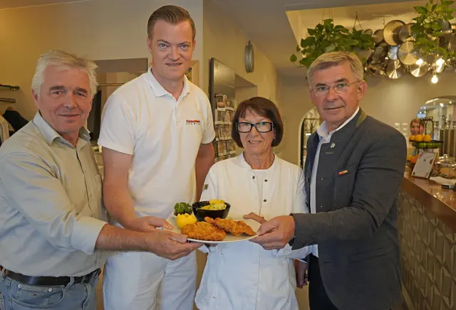 Eine kleine Gruppe Menschen hält einen Teller mit Schnitzel in die Kamera.