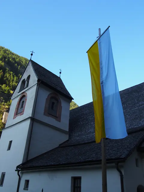 Eine gehisste Kirchenfahne weht im Außenbereich direkt vor dem Kirchturm am Lueg.