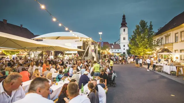 Menschen feiern auf aufgestellten Tisch- und Bankgarnituren auf einem Hauptplatz.