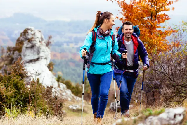 Sportliches Paar mit Wanderstöcken besteigt einen Berg.