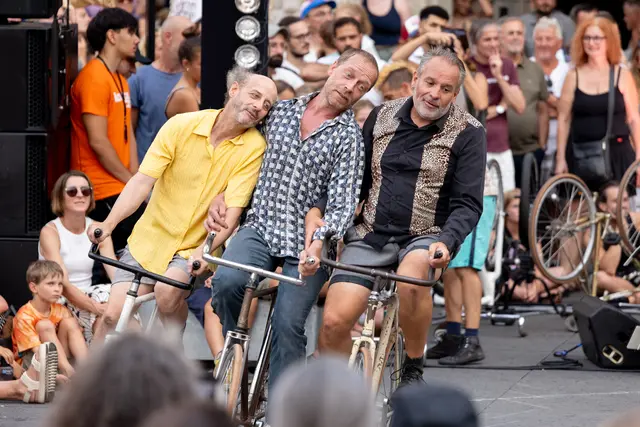 Drei Männer fahren Fahrrad und lehnen sich dabei aneinander an.