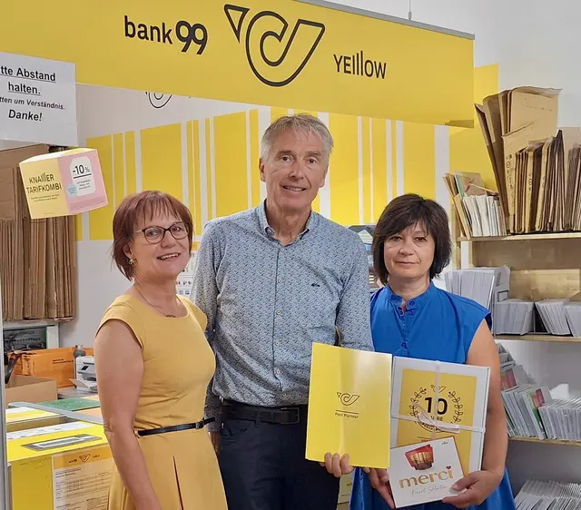Drei Menschen mit einer Urkunde und dem Logo der Post sind zu sehen.