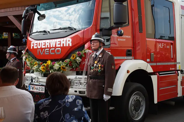 Feuerwehrauto mit zwei Feuerwehrkameraden und Bevölkerung