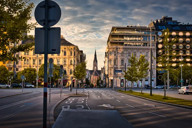 Blick entlang der Argentinierstraße in Wien während der Goldenen Stunde am Abend. Die Pfarrkirche St. Elisabeth erhebt sich zwischen historischen und modernen Gebäuden, während das warme Licht und der wolkenreiche Himmel die nahezu leere Straße stimmungsvoll in Szene setzen.