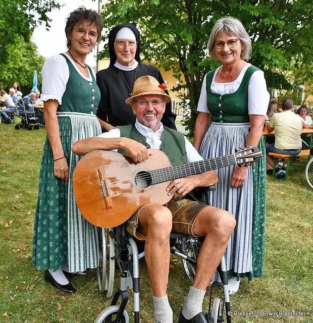 Hubert Tröbinger beim „Probesitzen“ auf einem Rollstuhl umrahmt von Traudi, Renate und Schwester Herma 

