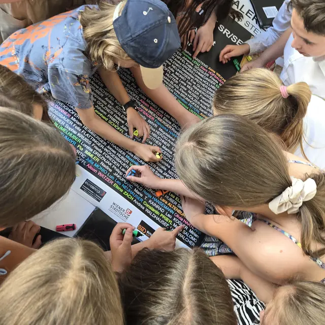 Die Kinder und Jugendlichen bei der Farbmarkierung ihrer Namen am Ausstellungsplakat. Dieses Werk wird als Gemeinschaftskunstwerk im Herbst als Benefiz für das "Weihnachtswunder" versteigert. | Foto: JAG