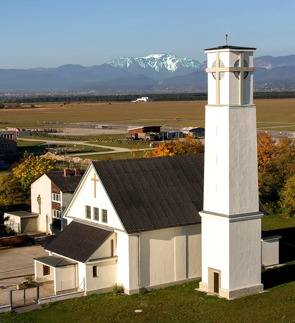 Die römisch katholische Kirche der Pfarrgemeinde St.Anton am Flugfeld mit dem Militärflugplatz und dem Schneeberg im Hintergrund.