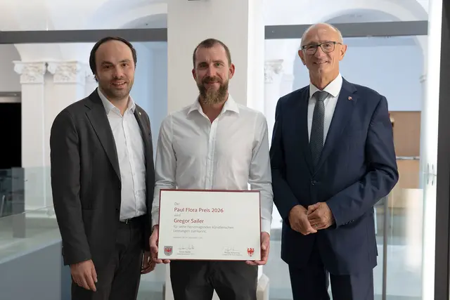 Gregor Sailer wurde im TAXISPALAIS Kunsthalle Tirol mit dem Paul-Flora-Preis 2026 ausgezeichnet. Überreicht wurde der mit 10.000 Euro dotierte Preis von Landeshauptmann Anton Mattle (re.) und Südtirols Kulturlandesrat Philipp Achammer (li.). | Foto: Land Tirol/Sidon