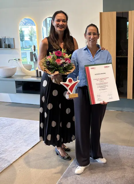 Zwei Frauen, eine mit Blumenstrauß, eine mit Urkunde
