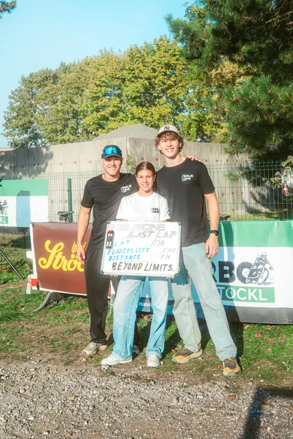 Ganzkörperaufnahme von drei jungen Menschen, welche ein Schild über sportliche Motivation in die Kamera halten und lächeln